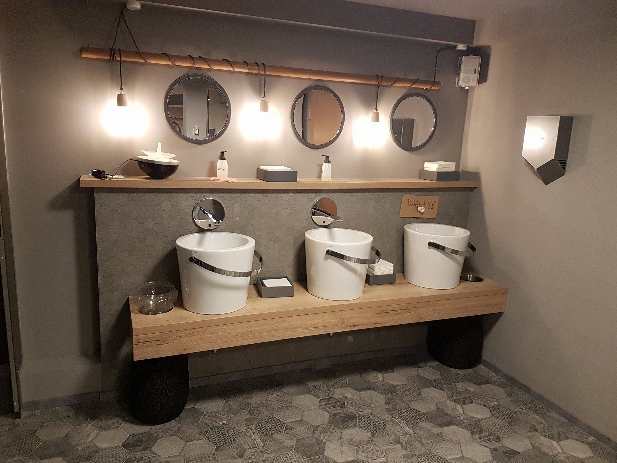 Bad mit drei Aufsatzbecken auf einem Holzwaschtisch, runden Spiegeln und Wand in Betonoptik