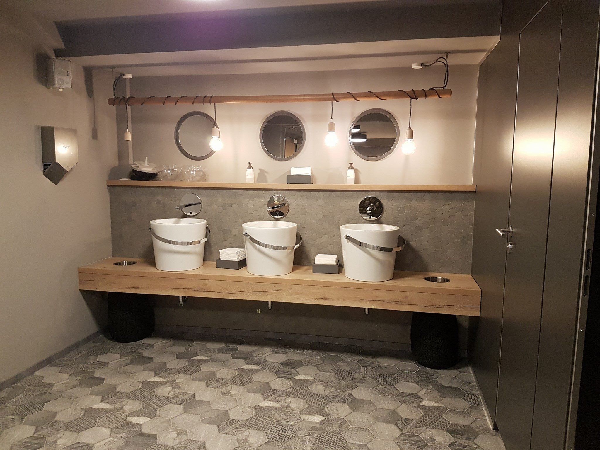 Badezimmer mit langem Holz-Waschtisch, drei Aufsatzbecken und runden Spiegeln vor einer grauen Wand
