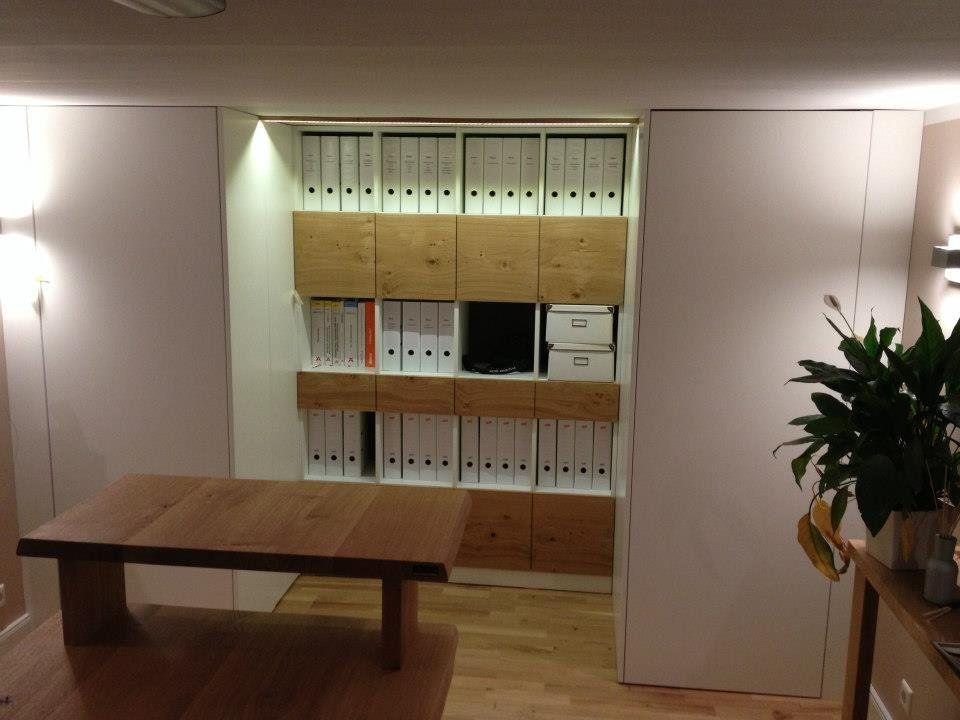 Büro mit weißer Regalwand mit Holzfronten und Ordnern, davor ein Holztisch