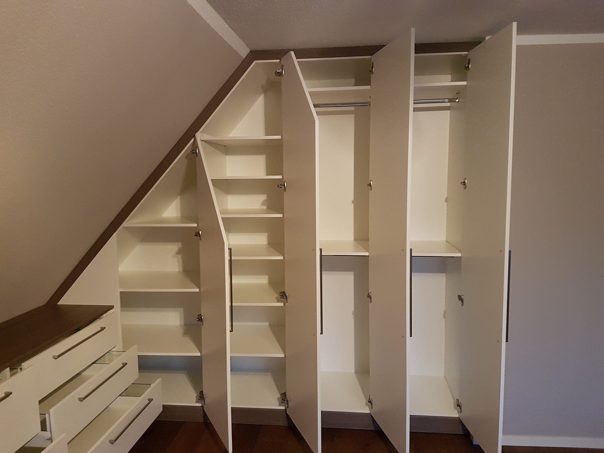 Weißer Einbauschrank unter einer Dachschräge mit geöffneten Türen, Regalen und Kleiderstange