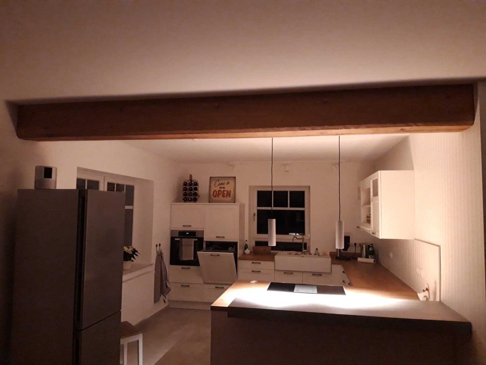 Weiße Küche mit Theke und Holzbalken an der Decke, abends beleuchtet