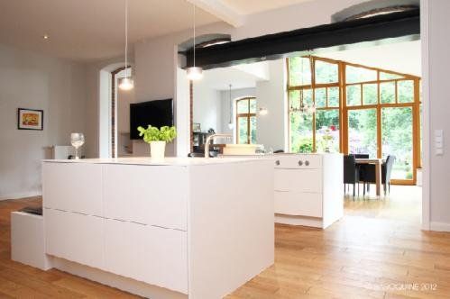 Weiße Küche mit Kochinsel in einem offenen Wohnraum mit Holzboden und Wintergarten