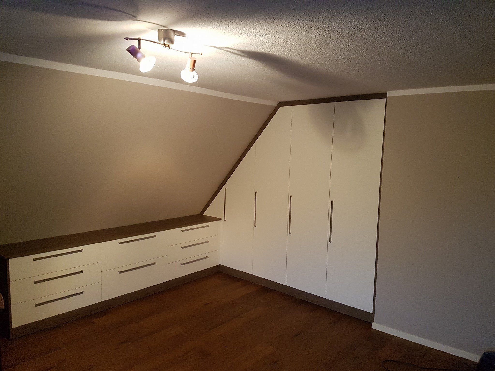 Weiße Einbauschränke mit Schubladen unter einer Dachschräge, an der Decke Spots