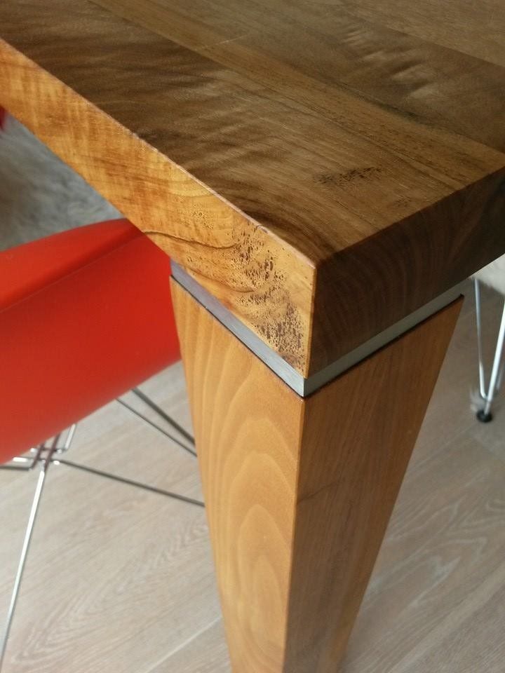 Nahaufnahme einer Massivholz-Tischplatte mit Astloch und einem Tischbein aus Holz mit Metallabschluss